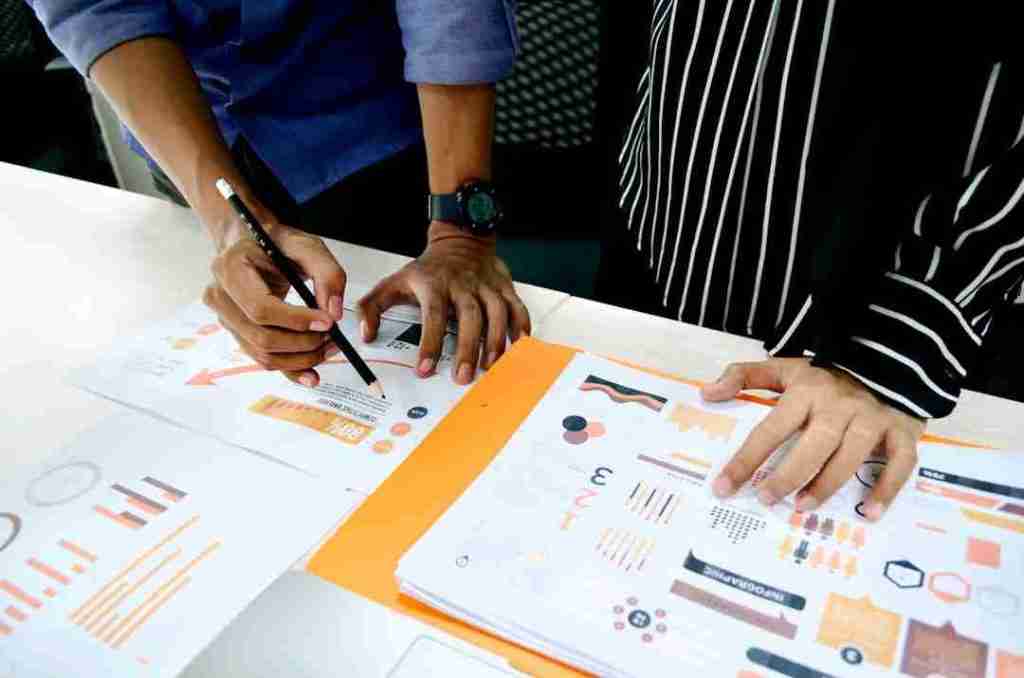 Transforming Insurance With Generative Ai Cxonxt | Two People Reviewing And Discussing Printed Financial Charts And Graphs Spread On A Table. One Person Is Pointing At A Document With A Pen. They'Re Deep In Conversation About Transforming Insurance With Generative Ai, Analyzing How It Can Revolutionize The Industry By Leveraging Advanced Data Insights.